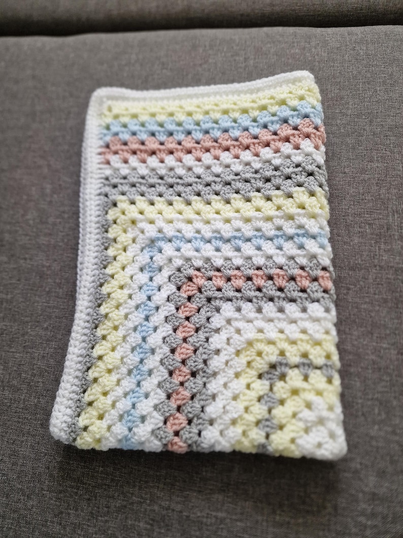 May include: A crocheted baby blanket with a white background and stripes of light blue, yellow, pink, and gray.
