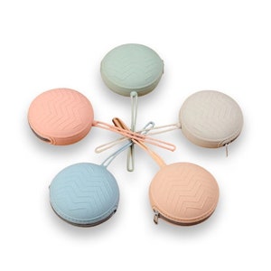 May include: Five round silicone zipper pouches in different colors, including light blue, pink, and beige. Each pouch has a zig-zag pattern and a small loop for attaching a key chain.