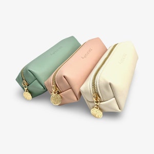 May include: Three zippered pouches in different colors: sage green, blush pink, and cream. Each pouch has a gold zipper and a gold charm with the word "perfectly" embossed on it.