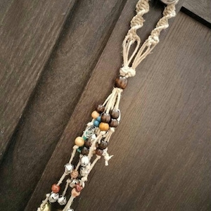 May include: A macrame doorstop with a brown, white, and blue beaded tassel and silver bells.