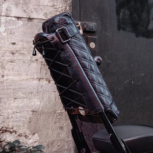 Puede incluir: Respaldo negro para motocicleta con un cojín de cuero acolchado y una placa de matrícula que dice "MOTOGAL". El respaldo está asegurado con cordones negros y una hebilla de metal. La placa de matrícula tiene el texto "JAN 2023 CAL".