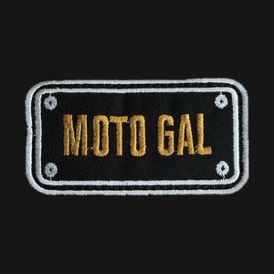 Könnte beinhalten: Ein gestickter schwarzer und weißer Aufnäher mit dem Text "MOTO GAL" in goldener Farbe.