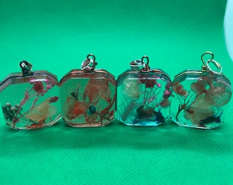 May include: Four square-shaped pendants with silver and gold accents. Each pendant contains pressed flowers and leaves encased in clear resin.