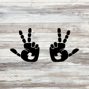 Puede incluir: Dos huellas de manos negras con una pequeña silueta de pato dentro de cada huella. Las huellas de manos están sobre un fondo de madera clara.