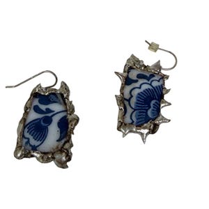 Pendientes de porcelana hechos a mano con diseño floral azul y blanco, con marco plateado en forma de pincho.