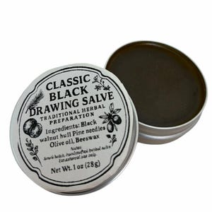 Puede incluir: Pequeño bote abierto de Classic Black Drawing Salve. La etiqueta presenta texto e ilustraciones botánicas. La pomada es de color marrón oscuro. Ingredientes: cáscara de nuez negra, agujas de pino, aceite de oliva y cera de abejas. Peso neto: 28g.