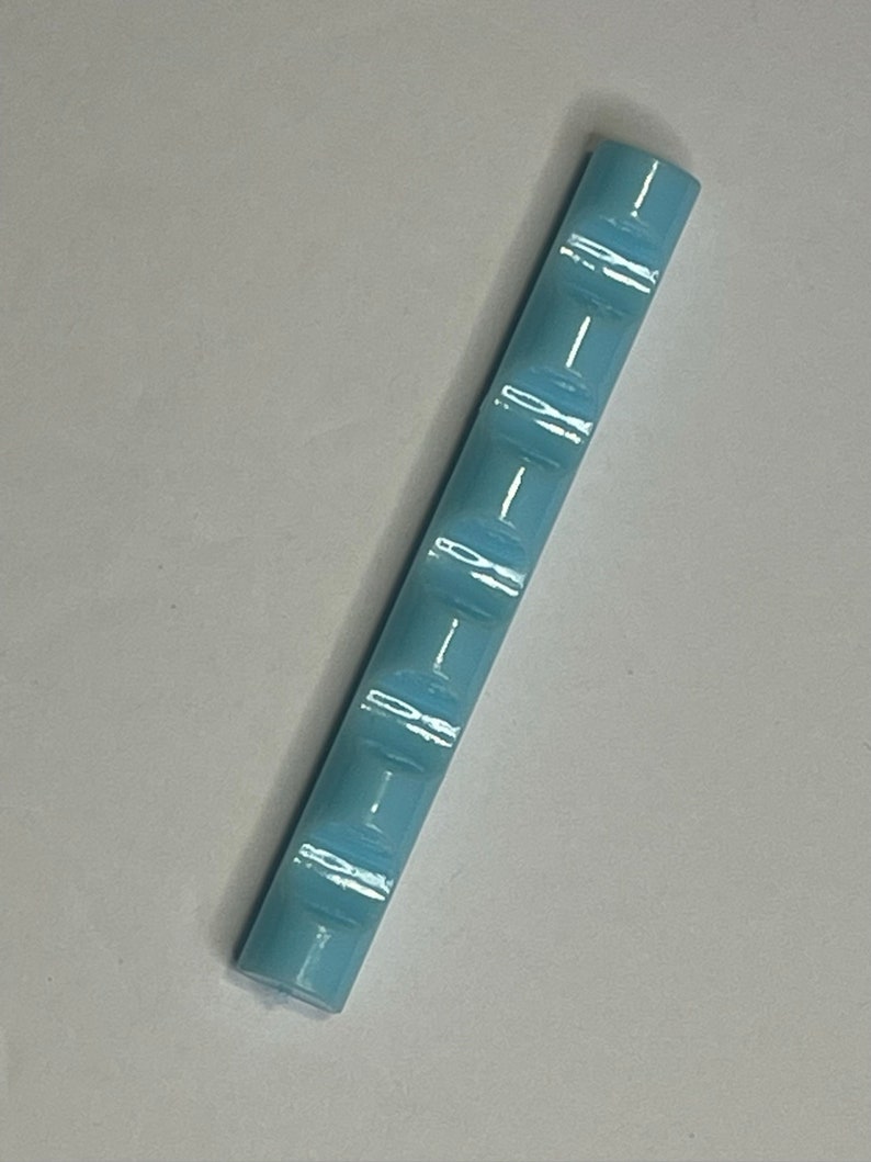 Może przedstawiać: Płytka ceramiczna w jasnoniebieskim kolorze z fakturowaną powierzchnią. Płytka ma kształt prostokąta i ma około 3,8 cm długości.