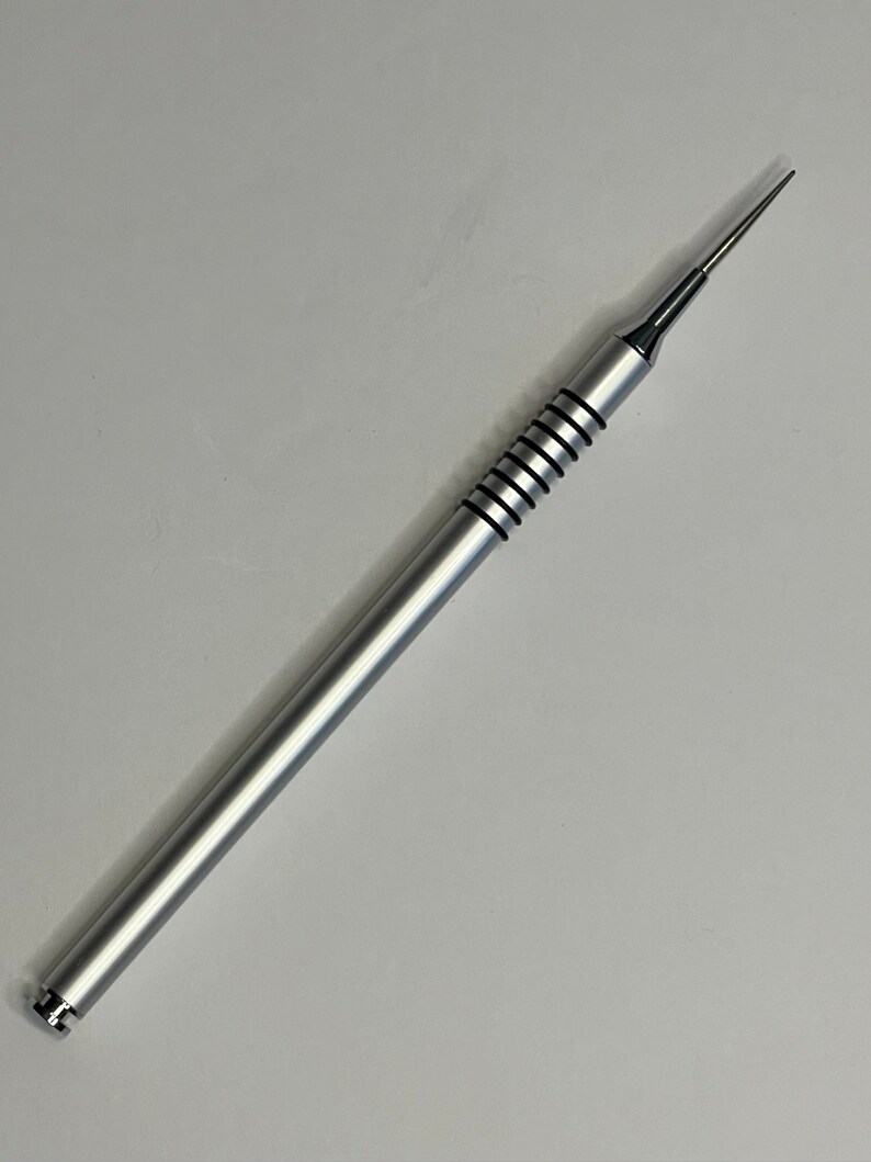 Może przedstawiać: Srebrne metalowe narzędzie z ostrym końcem i fakturowanym uchwytem. Narzędzie ma około 15 cm długości.