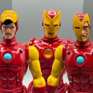 May include: Three Iron Man action figures. Each figure is red with yellow accents on the arms and helmet. The helmets are yellow with black eye slits. The center figure has a full helmet, while the other two have face masks.