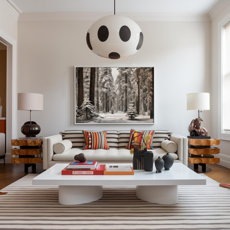 K&ouml;nnte beinhalten: Ein wei&szlig;es Sofa mit gestreiftem Bezug und bunten Kissen steht in einem Wohnzimmer mit einem wei&szlig;en Couchtisch und einer schwarzen und wei&szlig;en Polka-Dot-Pendelleuchte dar&uuml;ber. Ein gerahmtes Foto eines schneebedeckten Waldes h&auml;ngt an der Wand hinter dem Sofa.
