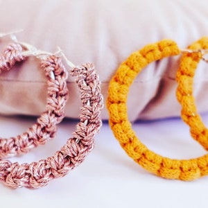 May include: Two pairs of crocheted hoop earrings. One pair is a light pink color and the other pair is a bright yellow color.