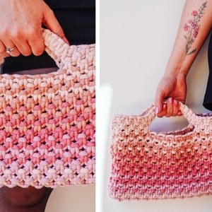 May include: A hand-held, woven tote bag with a gradient color scheme, transitioning from light beige to a vibrant pink. The bag features a rectangular shape with sturdy handles, showcasing a textured, knotted design.