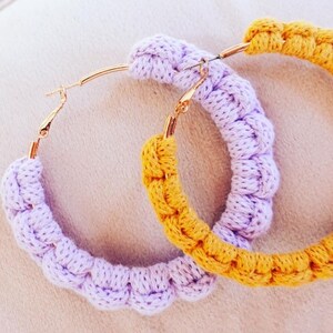 May include: A pair of large hoop earrings with a crocheted design. One earring is purple and the other is yellow.