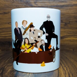 Könnte beinhalten: Eine weiße Keramiktasse mit einer bunten Illustration einer Gruppe von Personen in einem Boot. Die Personen tragen verschiedene Outfits, darunter einen braunen Trenchcoat, ein blau-weiß gestreiftes Hemd und einen schwarzen Anzug. Das Boot ist braun und hat eine gelbe Ente an der Seite. Der Text "TM" ist auf dem Boot sichtbar.