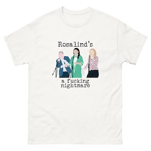 May include: White t-shirt with a graphic of three people with microphones. The text "Rosalind's a fucking nightmare" is printed above and below the illustration in black font. The t-shirt is made of a soft, comfortable material.