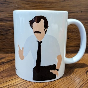 Könnte beinhalten: Weiße Keramiktasse mit einer Cartoon-Illustration eines Mannes mit Schnurrbart, der ein weißes Hemd und eine schwarze Krawatte trägt. Die Tasse hat einen Henkel und ist für heiße oder kalte Getränke geeignet.