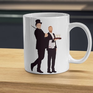 Könnte beinhalten: Weiße Keramiktasse mit einer Schwarzweißillustration von zwei Männern. Ein Mann trägt einen Zylinder und hält einen Stock. Der andere Mann hält ein Tablett mit Gläsern Champagner.