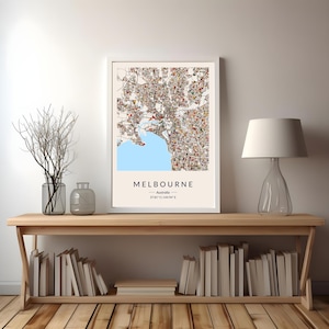 May include: A framed map print of Melbourne, Australia, with a light blue bay and colorful city details. The print includes the city name and coordinates. The artwork is displayed on a wooden shelf with books and decorative items.