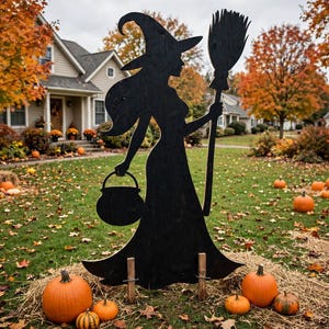 Peut inclure: Une silhouette noire découpée représentant une sorcière portant un chapeau pointu, tenant un balai dans une main et un chaudron dans l'autre. La figurine est fixée sur deux piquets en bois et posée sur une pelouse parsemée de citrouilles orange.