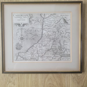 May include: A black and white antique map of Cardigan, Wales, with the text "CARDIGAN Comitatus pars Olim DIMETARVM" in the upper left corner. The map shows the surrounding areas of Merioneth, Montgo, Radnor, Brecenoc, and Carmar.