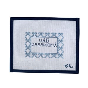 May include: A rectangular, off-white needlepoint with a navy blue border. The center features the words "wifi password" in a blue stitched frame. A small blue stitched design is in the lower right corner.