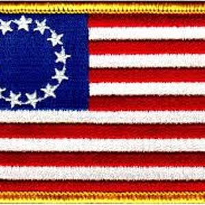 May include: Embroidered patch featuring the American flag design. The patch has a blue field with a circle of 13 white stars, and red and white stripes. The patch is rectangular with a gold border.