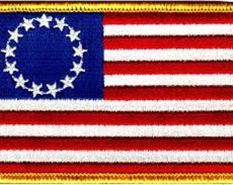 Peut inclure: Écusson brodé représentant le drapeau américain. Le patch a un champ bleu avec un cercle de 13 étoiles blanches et des rayures rouges et blanches. Le patch est rectangulaire avec une bordure dorée.