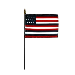 Puede incluir: Una pequeña bandera estadounidense con un diseño único. La bandera presenta un campo negro con estrellas blancas, rayas rojas y blancas, y una raya negra y roja. Montada en un mástil negro con un adorno dorado.