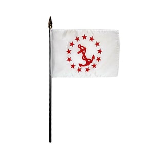 Könnte beinhalten: Eine kleine weiße Flagge mit einem roten Anker, umgeben von roten Sternen. Die Flagge ist an einer schwarzen Stange mit einer goldfarbenen Speerspitze befestigt. Die Flagge ist wahrscheinlich eine Staats- oder Schifffahrtsflagge.