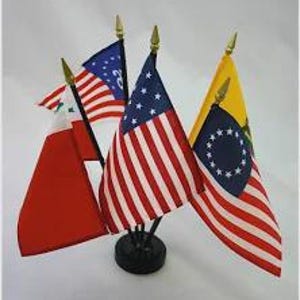 May include: A display of miniature flags, including the American flag with red and white stripes and blue stars, and other flags with various designs. The flags are mounted on black stands with gold-colored finials.