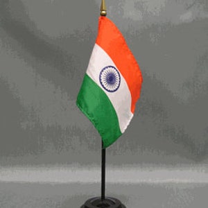 May include: A small desk flag of India, featuring the national flag's orange, white, and green stripes with the Ashoka Chakra in the center. The flag is mounted on a black stand with a gold-colored finial.