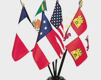 Może przedstawiać: Zestaw miniaturowych flag na czarnych podstawkach. Flagi reprezentują różne kraje i regiony, w tym Stany Zjednoczone i Francję. Flagi są czerwone, białe, niebieskie i zielone, ze złotymi zakończeniami.