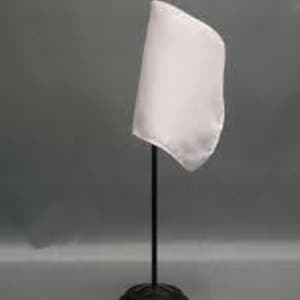 Puede incluir: Una pequeña bandera blanca sobre un soporte negro con una punta dorada. La bandera está hecha de un material liso y está ligeramente curvada. El soporte tiene una base redonda.