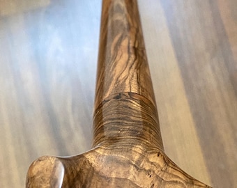 May include: A polished wooden walking stick featuring a smooth, curved handle and a long, straight shaft. The wood displays a rich, dark brown grain with swirling patterns and a glossy finish that highlights the natural texture of the timber.