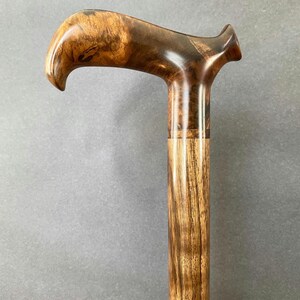 May include: A wooden walking cane with a curved handle. The handle is made from dark brown burl wood, and the shaft has a lighter, striped wood grain. This cane is a stylish mobility aid, demonstrating fine craftsmanship and natural materials.