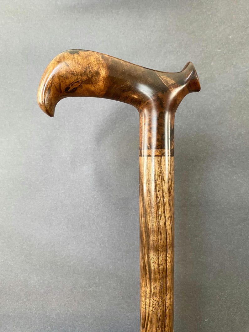 May include: A wooden walking cane with a curved handle. The handle is made from dark brown burl wood, and the shaft has a lighter, striped wood grain. This cane is a stylish mobility aid, demonstrating fine craftsmanship and natural materials.