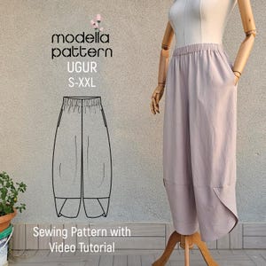 Puede incluir: Un pantalón de pierna ancha de color lila claro sobre un maniquí de madera. El pantalón tiene bolsillos y un dobladillo único. La imagen también muestra un patrón de costura con el texto "modella pattern UGUR S-XXL" y "Sewing Pattern with Video Tutorial."