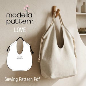 Może przedstawiać: Beżowa torba typu tote z dwoma paskami na ramię i bocznymi sznurkami wisi na drewnianym haczyku. Obraz zawiera tekst modella pattern LOVE oraz czarno-biały rysunek liniowy torby z napisem Sewing Pattern Pdf.