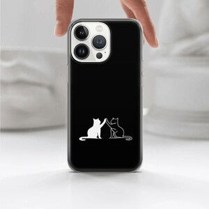 Puede incluir: Una funda de tel&eacute;fono negra con un contorno blanco de dos gatos d&aacute;ndose la mano. La funda del tel&eacute;fono tiene una parte posterior transparente y una parte delantera negra.