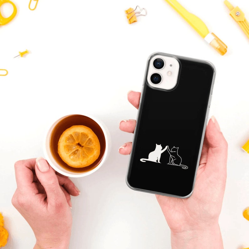 Puede incluir: Una funda de tel&eacute;fono negra con la parte posterior transparente y un contorno blanco de dos gatos d&aacute;ndose la mano.