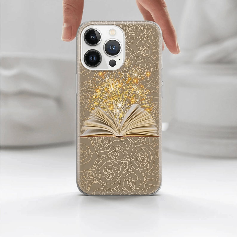 May include: A clear phone case with a gold design of roses and an open book with sparkling lights coming from it.