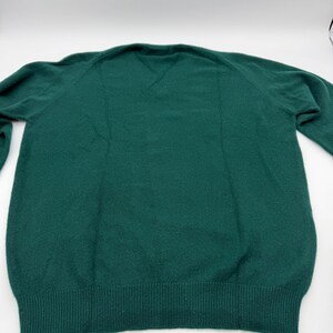 Puede incluir: Un su&eacute;ter de manga larga en color verde oscuro s&oacute;lido con cuello en V y pu&ntilde;os y dobladillo de punto acanalado. La prenda est&aacute; confeccionada con un tejido de punto suave y texturizado, con mangas ragl&aacute;n y un dise&ntilde;o limpio y sin estampados.
