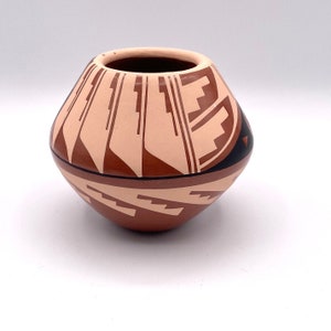 May include: A small, hand-painted pottery vase with a geometric design in shades of brown, pink, and black. The vase has a rounded base and a wide opening.