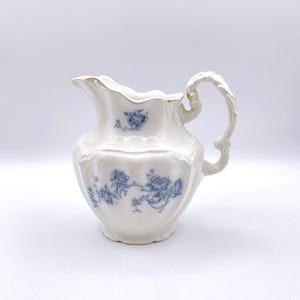 May include: A white porcelain creamer with a blue floral pattern and a gold-trimmed handle.