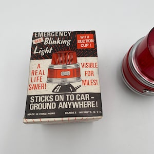 May include: Red blinking emergency light with a suction cup. The box reads "Emergency Red Blinking Light", "With Suction Cup!", "A Real Life Saver!", "Visible For Miles!", "Sticks On To Car - Ground Anywhere!", "Made In Hong Kong", "Dandee Imports, N.Y.C."