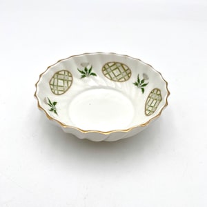 May include: A white porcelain saucer with a gold rim and green and white floral design.