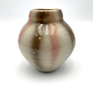 May include: A small, round ceramic vase with a narrow neck. The vase features a color scheme of brown, pink, and off-white vertical stripes. The surface has a crackled texture, adding to its handmade aesthetic. The vase is suitable for displaying small flowers or as a decorative item.