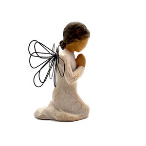 May include: A kneeling figurine of a person with dark hair, wearing a white dress, and praying with hands clasped. The figurine has wire wings and a textured, off-white finish. The figurine is on a white background.