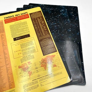 May include: A stack of vintage sky maps. The top map is yellow with the title "TWELVE SKY MAPS" and a world map graphic. The other maps are black with white star patterns. The maps are educational and feature astronomical information.