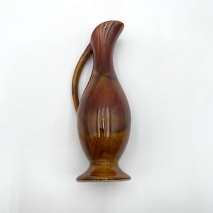 May include: A small brown and orange ceramic pitcher with a flared lip and a handle. The pitcher has a glossy finish and a slightly textured surface.